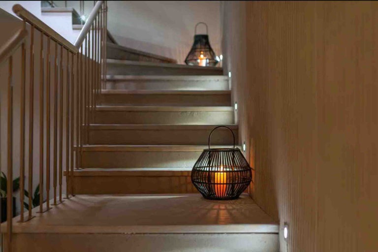 Scară modernă din lemn iluminată cu spoturi LED încastrate în perete și felinare decorative cu lumânări.