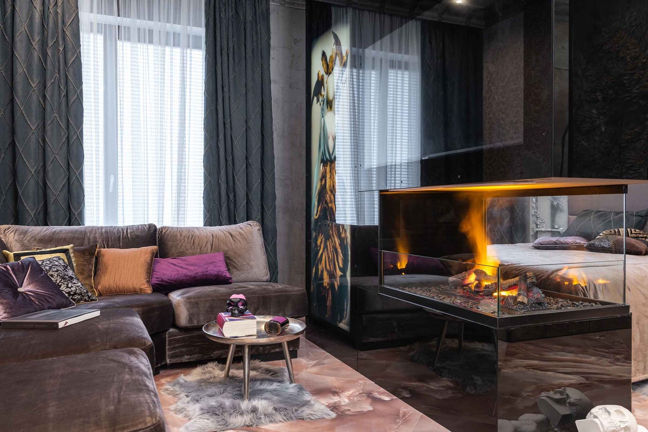 Sufragerie modernă cu canapea de catifea, perne decorative și măsuță pe un covor de blană. Șemineu electric din sticlă cu flăcări.
