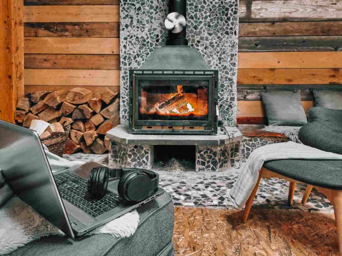 Cameră de zi confortabilă cu șemineu, grămadă de lemne, laptop și căști pentru o atmosferă relaxantă.