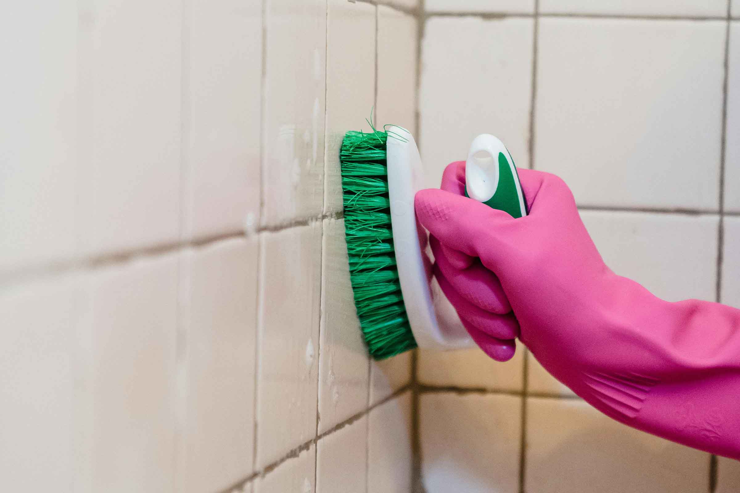 O mână cu o mănușă de protecție curăță faianța cu o perie