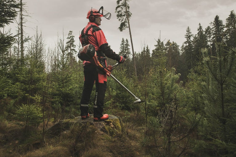 Bărbat cu motocoasă în peisaj forestier, echipat cu îmbrăcăminte de protecție
