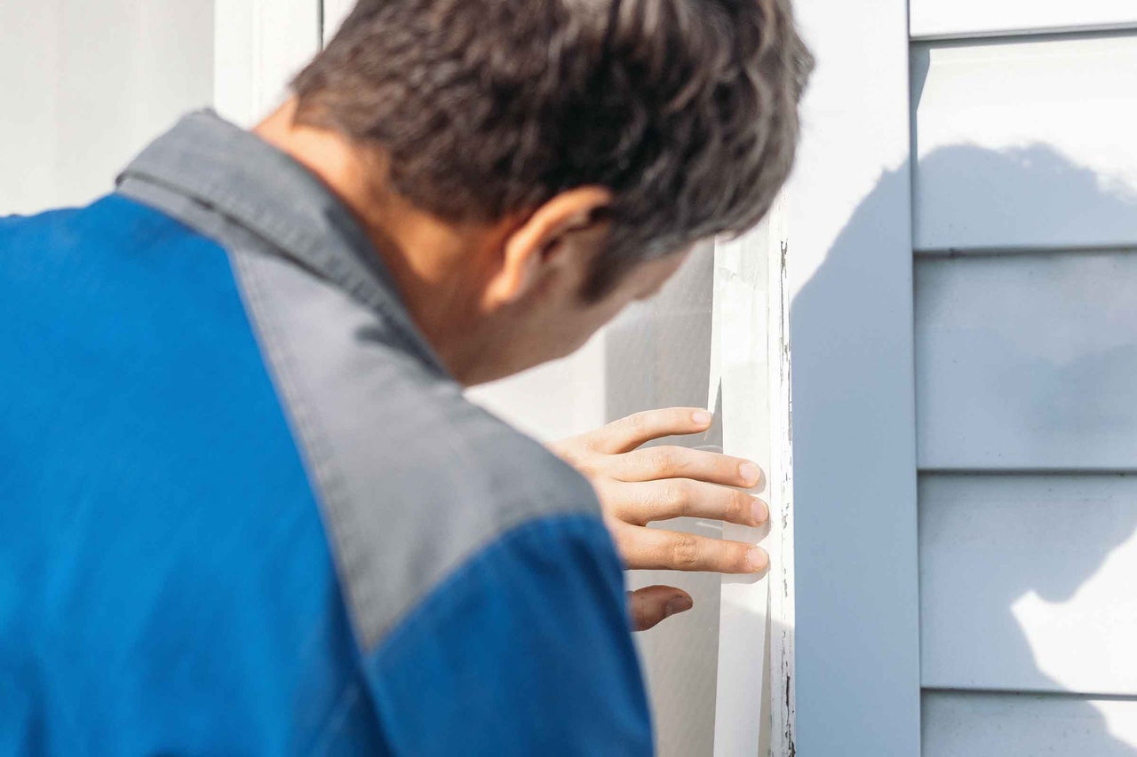 O persoană inspectează un perete de casă pentru daune.