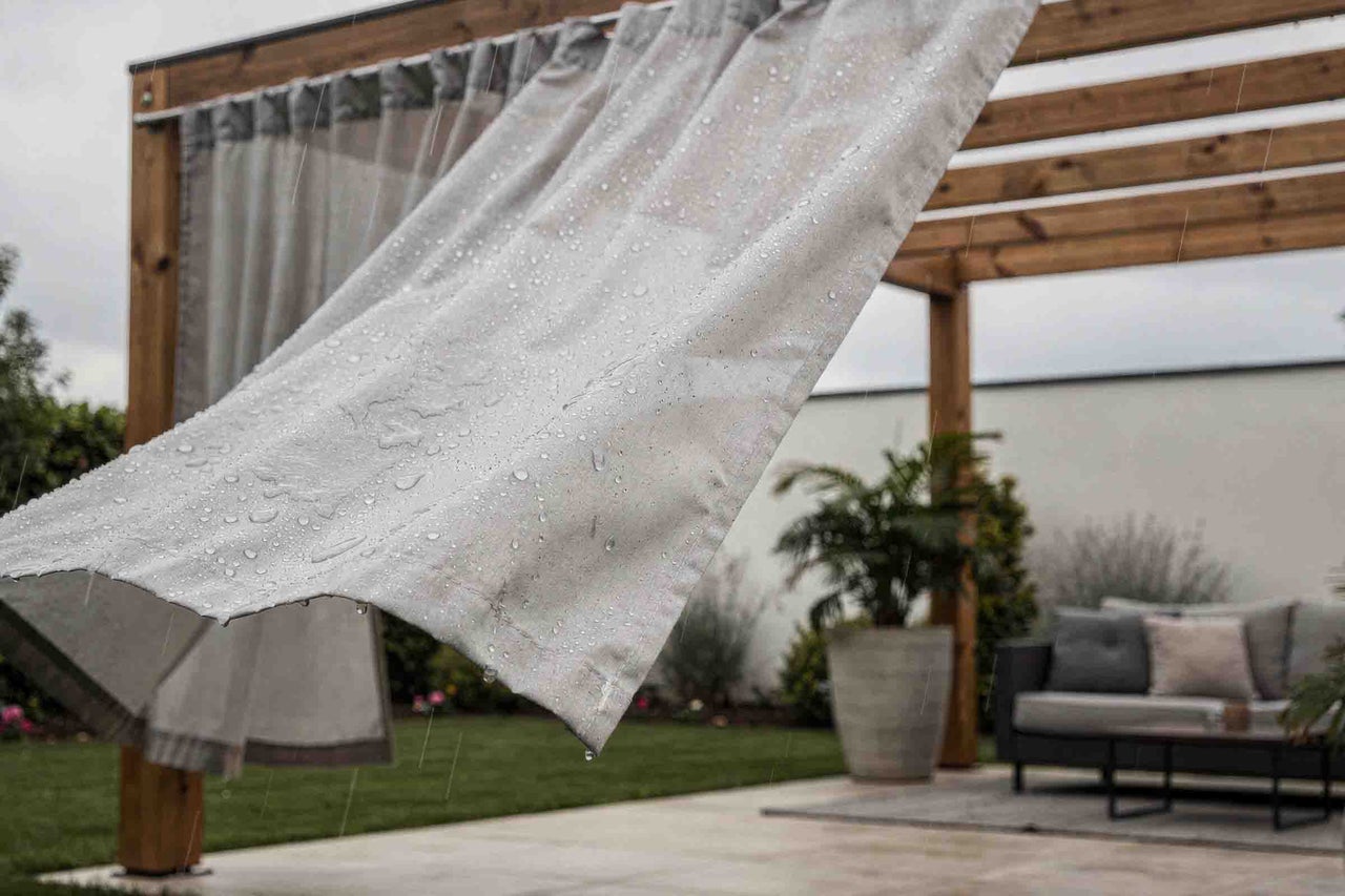 Perdea de exterior rezistentă la apă cu picături de ploaie pe o pergolă din lemn într-o grădină modernă cu mobilier și plante.