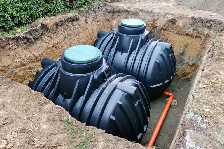 Două rezervoare subterane din plastic negru cu capace verzi instalate într-o groapă cu o țeavă de legătură portocalie.