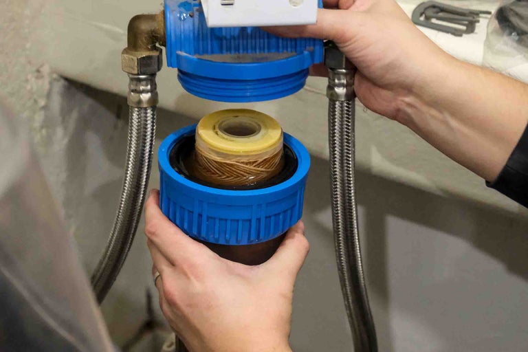 Înlocuirea unui cartuș de filtru de apă într-o carcasă albastră cu furtunuri metalice flexibile.