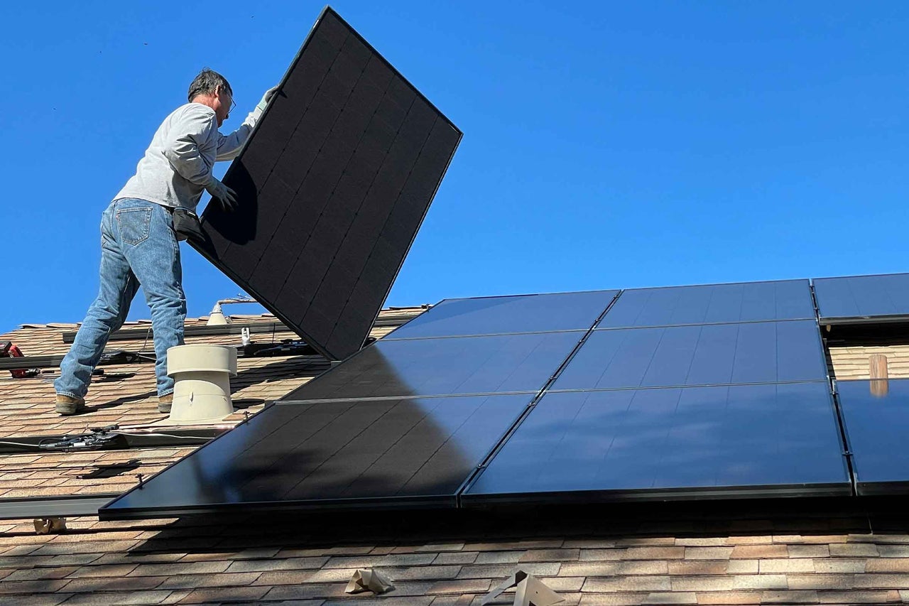 Un meșter instalează panouri solare pe un acoperiș pentru generarea de electricitate.