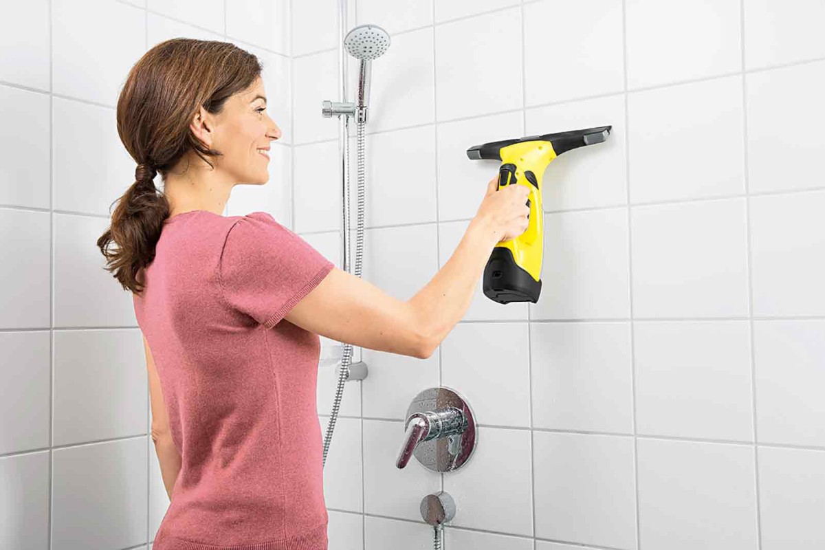 Femeie șterge faianța cu un aspirator de geamuri fără fir în baie.