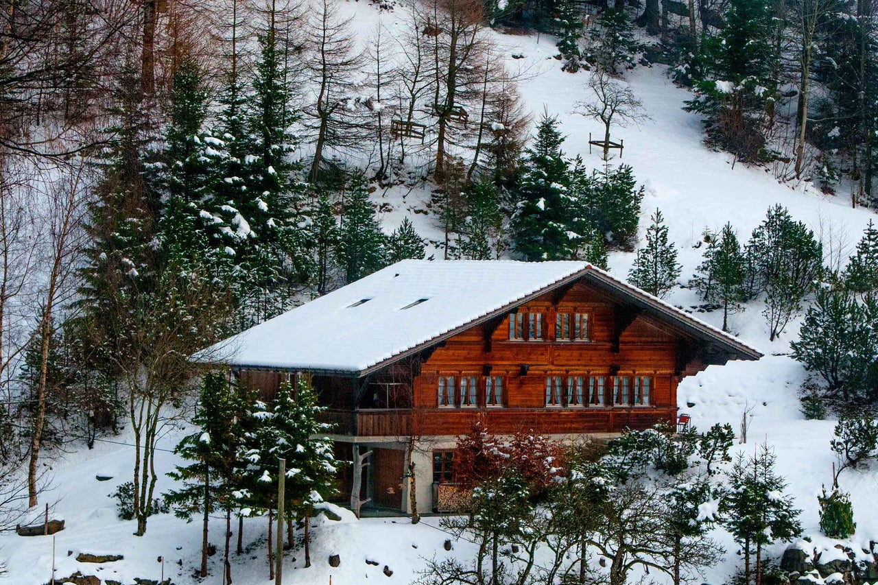 Casă din lemn iarna cu zăpadă pe acoperiș și copaci