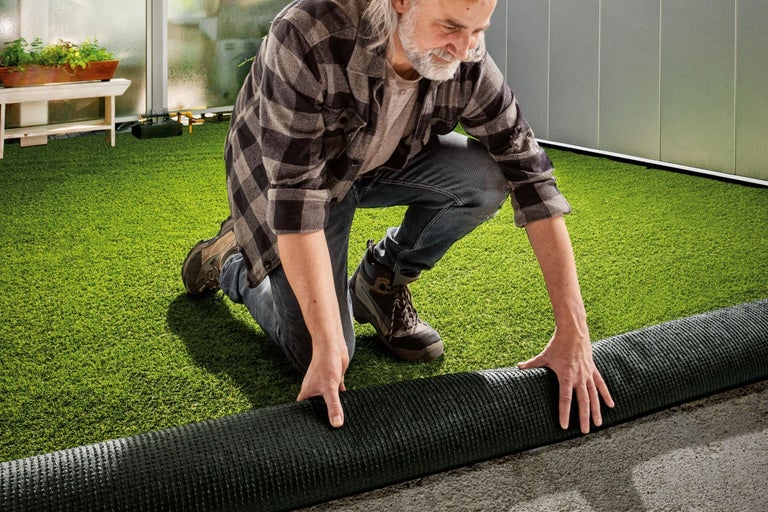 Bărbat care așterne gazon artificial într-un spațiu exterior
