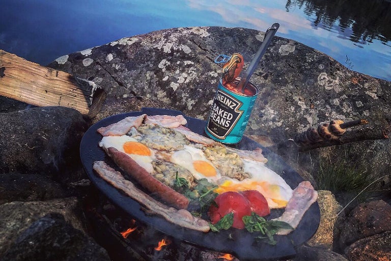 Mic dejun cu ouă, bacon, cârnați, roșii și fasole gătite în natură.