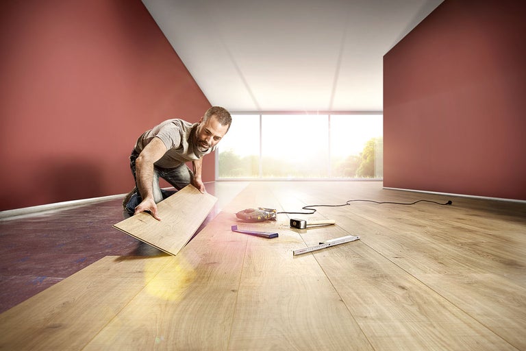 Un bărbat instalează laminat într-o cameră luminoasă cu unelte