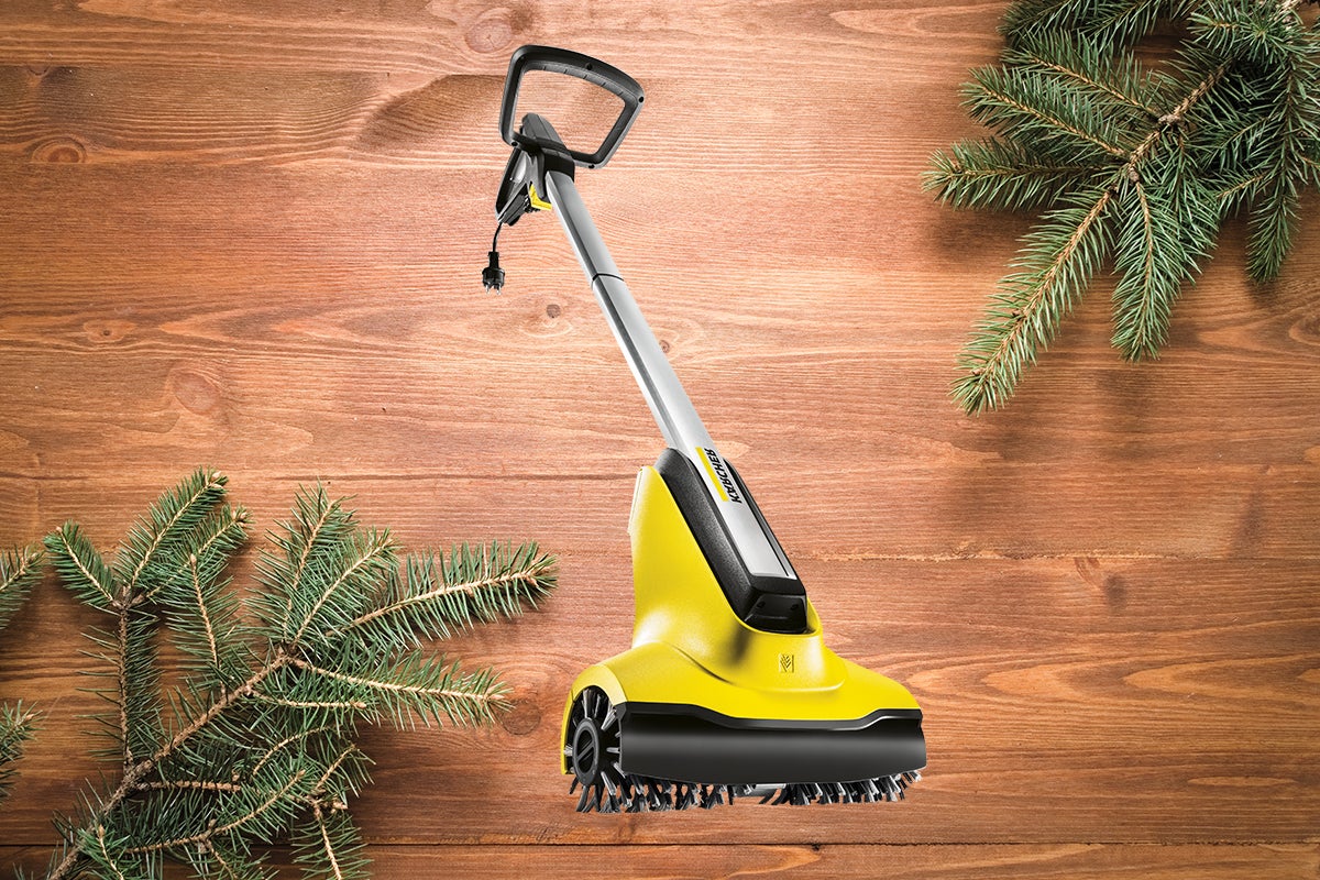 Mătură cu acumulator Kärcher pe fundal de lemn cu ramuri de brad