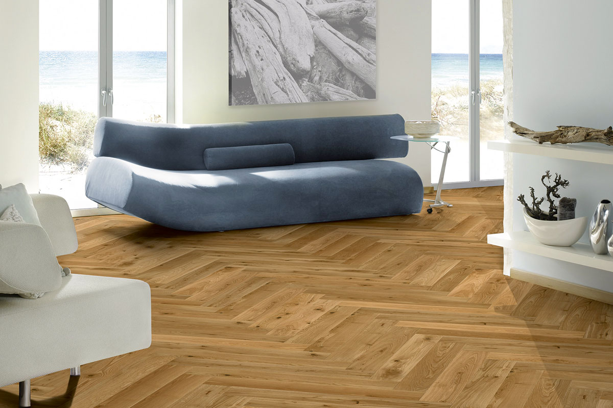 Cameră de zi cu podea de parchet în model herringbone, canapea și fereastră cu vedere la mare.