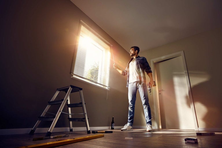 Bărbat care operează jaluzele cu o șurubelniță fără fir în mână, scară și instrumente în cameră.