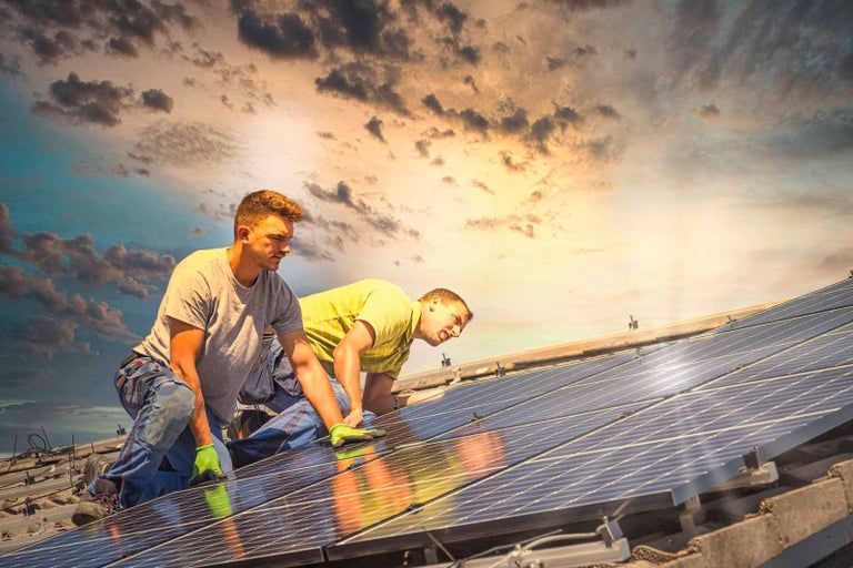 Doi instalatori montează panouri solare pe un acoperiș.