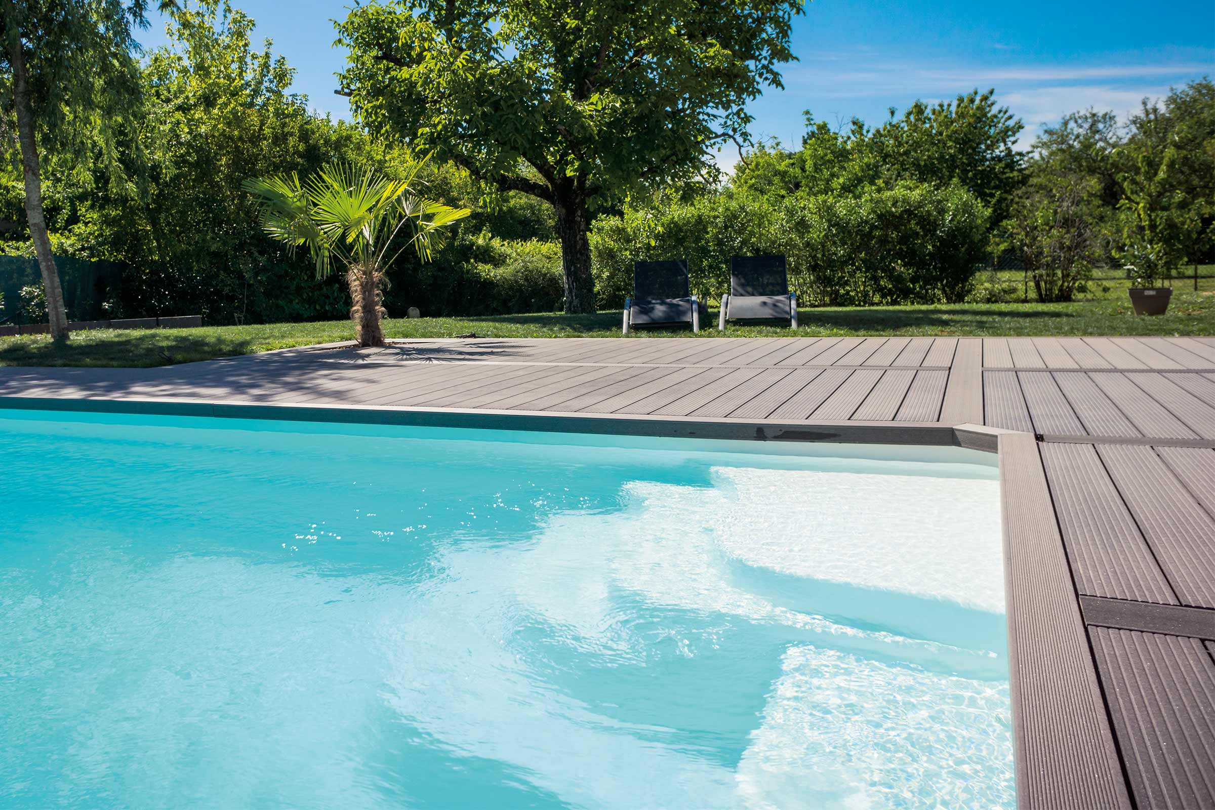 Scenă cu o piscină, terasă din lemn și două șezlonguri în fundal