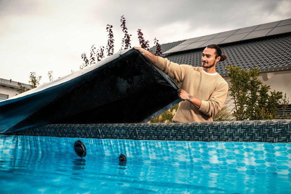 Bărbat îndepărtând prelata piscinei de pe piscina supraterană din grădină