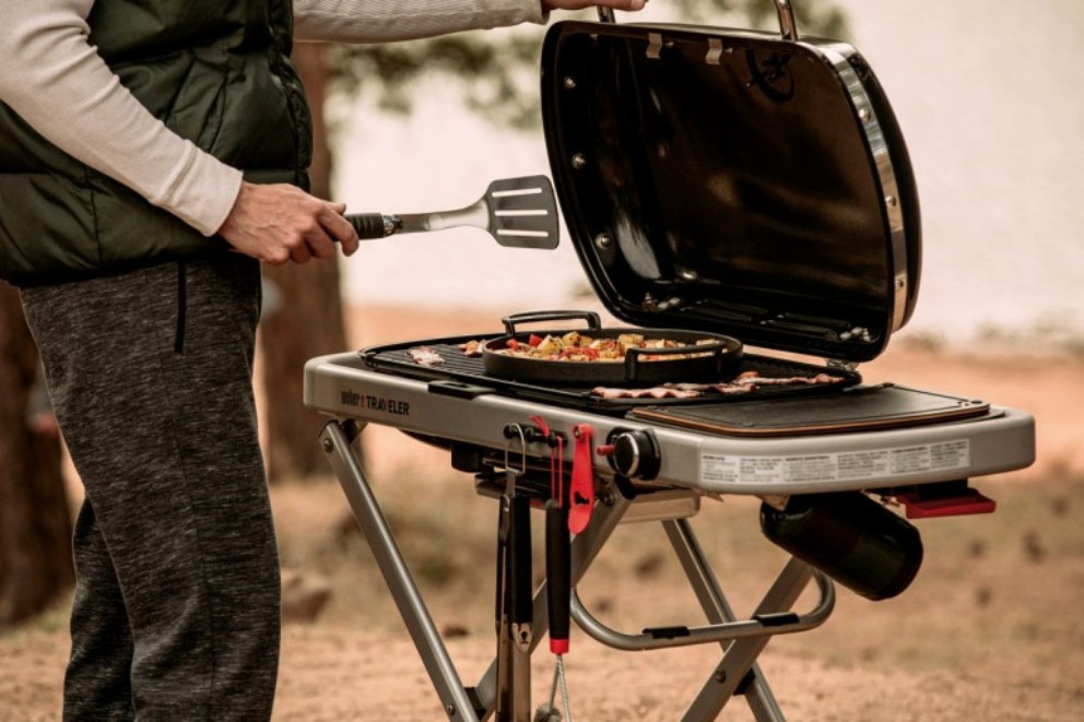 Bărbat care face grătar în aer liber pe un grătar Weber Traveler.
