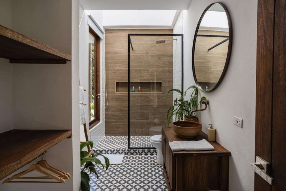 Baie în stil scandinav – mobilier din lemn, rafturi, umerașe, cabină de duș, podea mozaic, chiuvetă, oglindă rotundă, plantă, fereastră Baie în stil scandinav – mobilier din lemn, rafturi, umerașe, cabină de duș, podea mozaic, chiuvetă, oglindă rotundă, plantă, fereastră