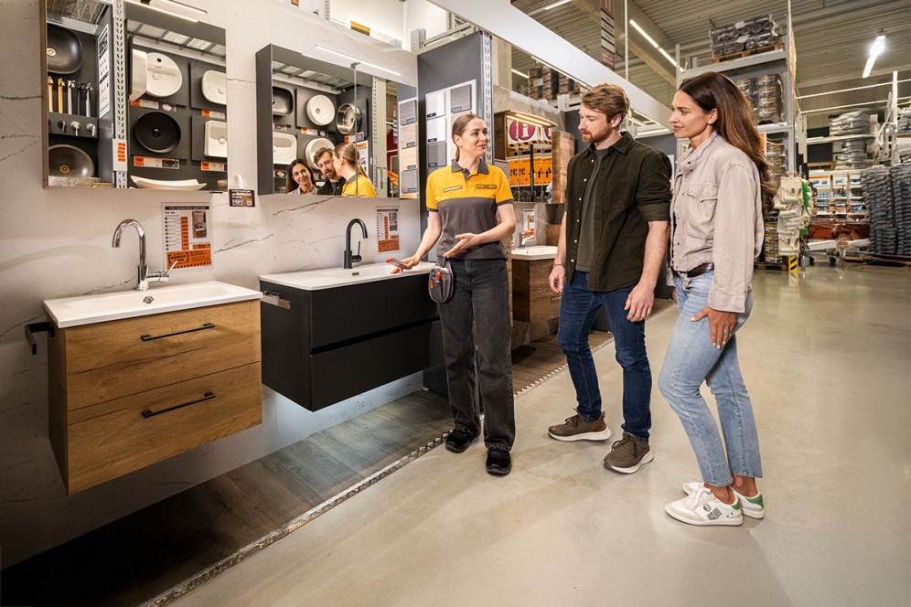 Expoziție de băi cu chiuvete, oglinzi și clienți în magazinul de bricolaj Hornbach