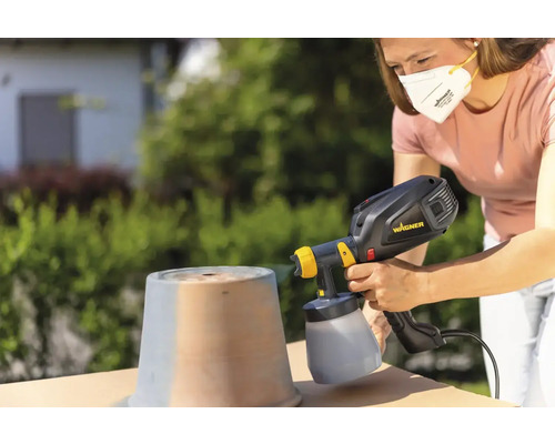 Femeie pulverizează vasul afară cu un sistem de pulverizare a vopselei