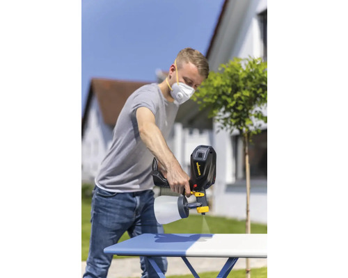 Un bărbat folosește un pistol de pulverizare pentru a vopsi o masă în aer liber.