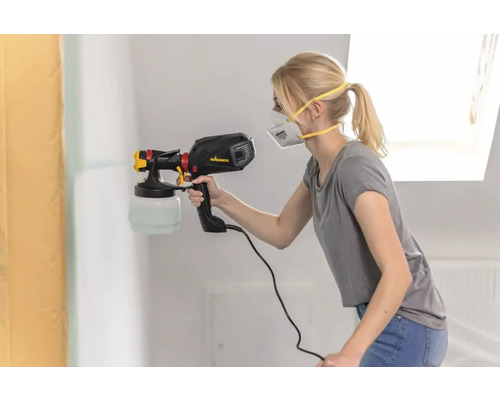O femeie pulverizează vopsea pe un perete cu un pulverizator de vopsea.