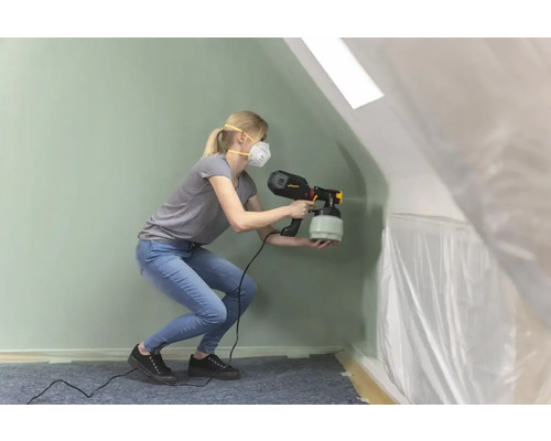 O femeie folosește un pulverizator de vopsea într-o cameră acoperită cu folie.