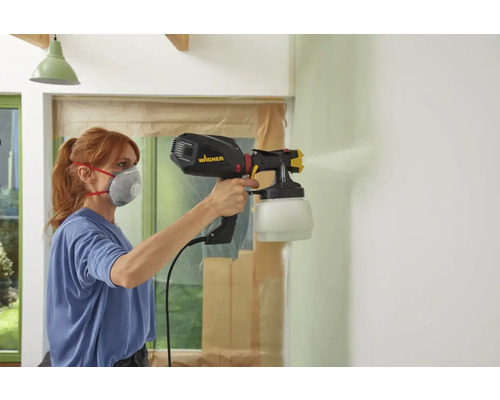 Femeie vopsește un perete cu un sistem de pulverizare a vopselei Wagner