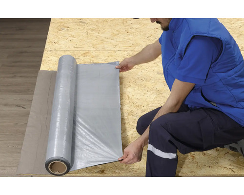 O persoană derulează folie de construcție pe o suprafață de lemn.