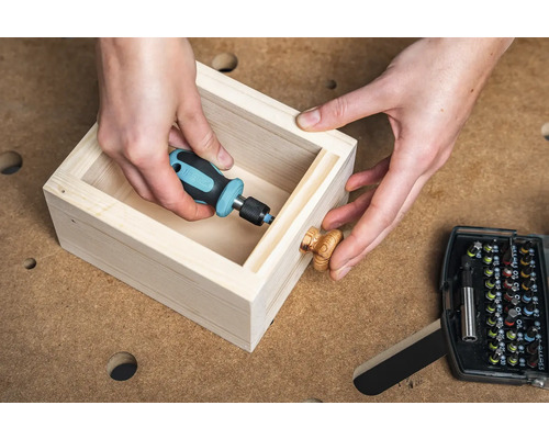 Artizanul fixează un buton de lemn pe un sertar cu o șurubelniță.