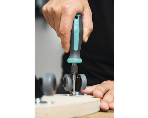 O persoană fixează o rolă pivotantă de o scândură de lemn cu o șurubelniță.