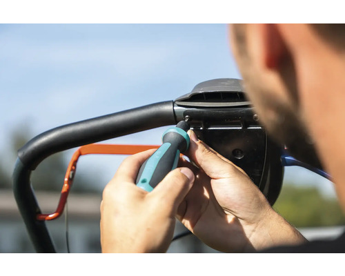 O persoană fixează mânerul unei mașini de tuns iarba cu o șurubelniță.