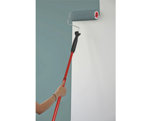 Vopseaua este aplicată pe un perete cu o rolă de vopsea și un mâner telescopic.