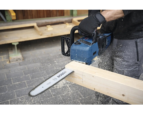 O persoană taie o scândură de lemn cu un motoferăstrău cu acumulator Bosch.