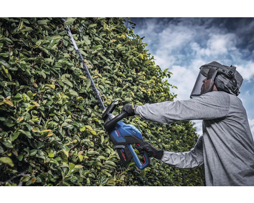 Bărbat cu vizieră de protecție tăind gard viu cu foarfecă de gard viu fără fir