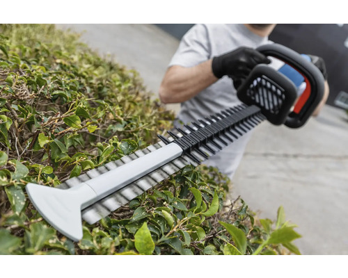 O persoană taie un gard viu cu o foarfecă de tuns gardul viu.