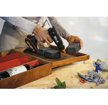 Pistol de lipit cu acumulator care fixează bucăți de spumă într-o cutie de lemn.