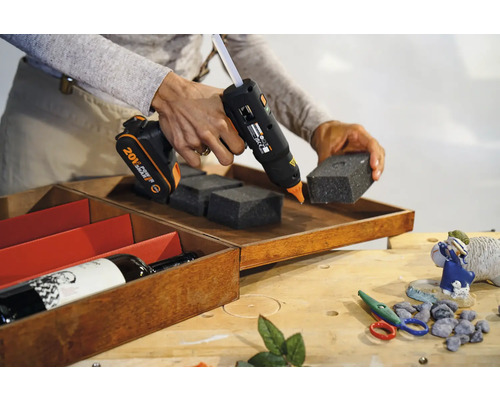 Pistol de lipit cu acumulator care fixează bucăți de spumă într-o cutie de lemn.