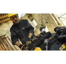 Un muncitor în construcții cu cască de protecție schimbă bateria unei scule electrice pe un șantier.