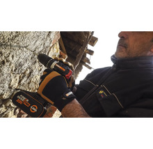 Un bărbat forează o gaură într-un zid de piatră cu o șurubelniță fără fir.