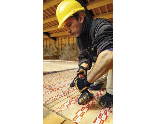 Meseriaș cu cască de protecție și șurubelniță cu acumulator instalând plăci izolatoare pe o podea de lemn.