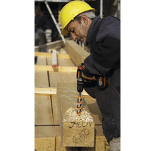 Un muncitor în construcții forează o grindă de lemn cu o bormașină cu acumulator.