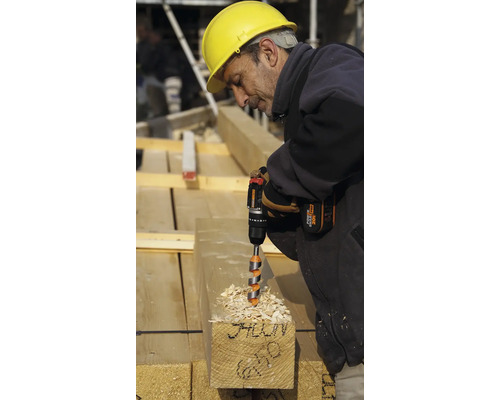 Un muncitor în construcții forează o grindă de lemn cu o bormașină cu acumulator.