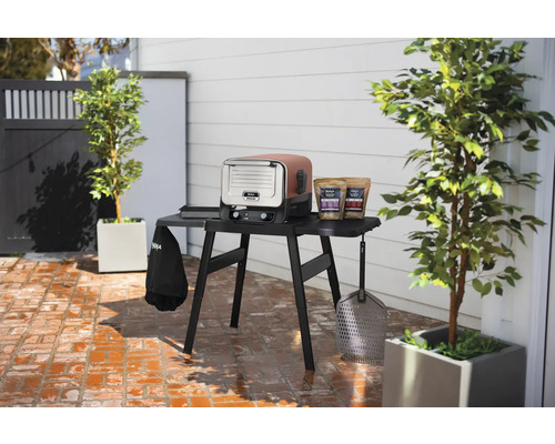 Scenă în aer liber cu un grătar electric Ninja Woodfire și accesorii pe o masă.
