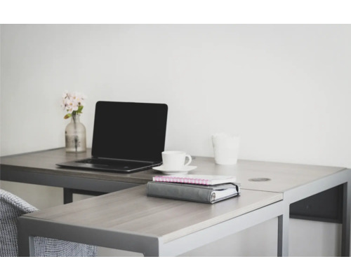 Un spațiu de lucru luminos cu birou, laptop, ceașcă, blocnotes și o vază mică cu flori.