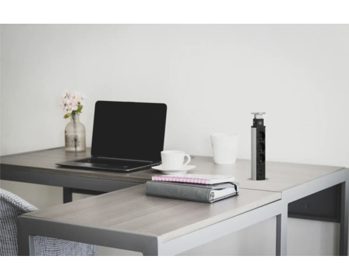 Birou cu laptop, ceașcă de cafea, blocnotes și coloană retractabilă de prize pe un birou.