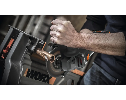 O persoană taie o țeavă de cupru cu o polizor unghiular fixată într-un banc de lucru. Logo WORX.