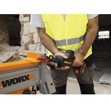 Un bărbat în vestă de siguranță taie cu un fierăstrău electric un fier de armare într-un atelier.