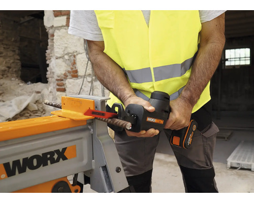 Un bărbat în vestă de siguranță taie cu un fierăstrău electric un fier de armare într-un atelier.